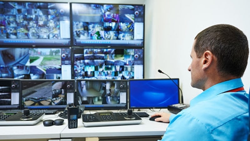 Man in campus security control center monitoring campus through video wall displaying live camera footage