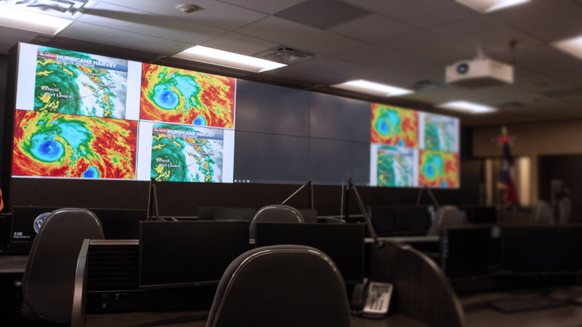 Sala di controllo vuota con radar meteorologici visualizzati su un grande videowall e postazioni di lavoro.