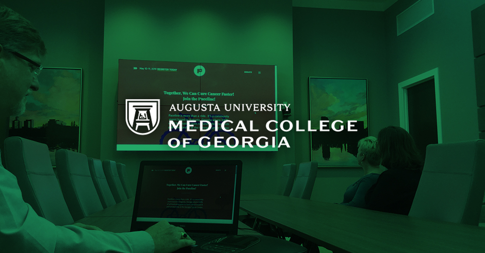 Sala riunioni del Medical College of Georgia, con un uomo che utilizza il suo computer portatile e Userful per visualizzare una pagina web su un video wall alle sue spalle con sovrapposizione verde e logo