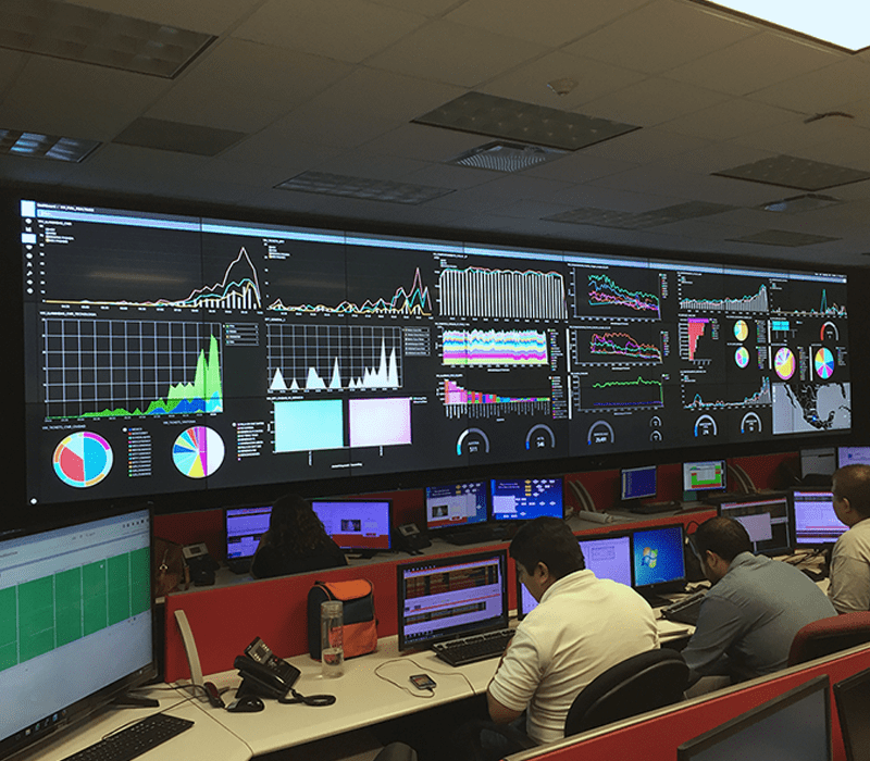 Dipendenti che lavorano in una sala di controllo su postazioni di lavoro con videowall che visualizzano cruscotti di dati
