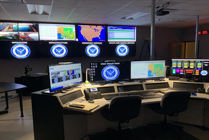 Sala di controllo EMA vuota, con postazione di lavoro e videowall per la visualizzazione di fotografie, dati e mappe.