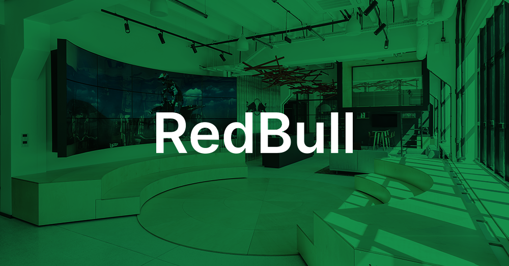 Lobby della sede centrale di Redbull Polonia, con area salotto con scalinata, reception e videowall curvo che mostra uno spot pubblicitario di Red Bull con sovrimpressione verde e il logo.